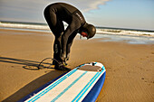 Ein männlicher Surfer, der Surfbrett-Leine zu seinem Knöchel bindet