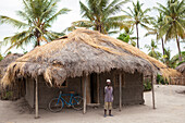 Ein Mann steht stolz vor seiner traditionellen Lehmhütte, die gerade mit einem Sonnenkollektor ausgestattet wurde, Tansania, Ostafrika, Afrika