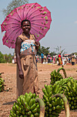 Eine Dame, die Bananen auf dem Markt verkauft, schützt sich vor der Sonne unter einem rosa Regenschirm, Ruanda, Afrika