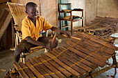 Ein Schuljunge, der Musik auf einem großen hölzernen Xylophon an seiner Grundschule in Ghana, Afrika spielt