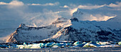 Winter view over frozen Jokulsarlon Glacier Lagoon showing blue icebergs covered in snow and distant mountains, South Iceland, Polar Regions