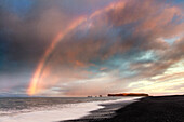 Fernsicht von Dyrholaey bei Sonnenaufgang mit Regenbogen, von Halsanefs Hellir Beach in der Nähe von Vik, Südisland, Polarregionen