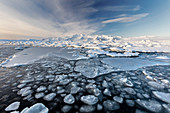 Frozen Jokulsarlon Glacial Lagoon im Winter mit Eis im Vordergrund und Schnee bedeckten entfernten Bergen, Südisland, Polargebiete