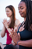 Photograph of two women meditating with eyes closed and hands clasped (Anjali mudra), Newport, Rhode Island, USA