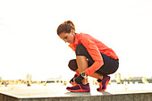 Female jogger tying shoes against clear sky, Boston, Massachusetts, USA