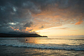 Surfers wait for waives as the sun sets behind the mountains in Hanalei Bay, Kauai, Hawaii