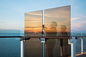 Paar fotografiert Sonnenuntergang von hinter Windschutz Fenster auf Deck 14 an Bord von Kreuzfahrtschiff Mein Schiff 6 (TUI Cruises), Ostsee, nahe Dänemark, Europa