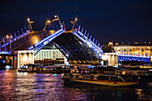 'Boats pass opened Dvortsovy bridge (Palace bridge) drawbridge on Neva river during ''White Nights'' with illuminated Kunstkamera Museum behind at night, St. Petersburg, Russia'