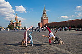 Young children play and perform cartwheels in Red Square with St. Basil's Cathedral and Moscow Kremlin wall behind, Moscow, Russia