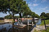 Couple with bicycles take rope ferry across canal, Klazienaveen, Drenthe, Netherlands