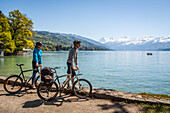 a couple of cyclists making a stop to contemplate lake thun and the mountain range, thun, canton of berne, switzerland