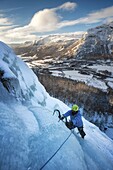 climber/mountaineer in the first rays of the sun climbing a blue ice cascade overhanging a snowy glacial valley, bottnebekken cascades, hemsedal, buskerud, norway