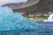 icebergs that separated from the glacier snouts in the fjord in front of the colorful wooden houses of the village of narsaq, greenland