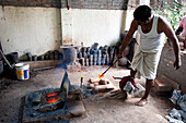 Man in white vest and dhoti, pouring molten bronze into clay mould, in Chola style lost wax bronze casting workshop, Thanjavur, Tamil Nadu, India, Asia