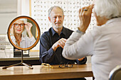 Optician assisting senior woman in choosing eyeglasses at store