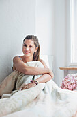 Porträt einer schönen Frau, die mit einer Decke auf dem Bett zu Hause sitzt