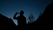 Silhouette man drinking water from bottle while standing on mountain at night
