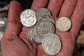 Hand hält neukaledonische Münzen die am Fuß eines Kreuzes auf einem Hügel hinterlassen wurden, Ile des Pins, Neukaledonien, Südpazifik
