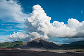 View from a distance to Mount Yasur volcano decked by brown and white clouds and surrounded by blue skies, Tanna Island, Vanuatu, South Pacific