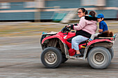 Woman rides with two young children on ATV all-terrain vehicle, Ulukhaktok (also Holman), Victoria Island, Northwest Territories, Canada, North America