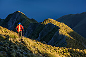 Woman hiking ascending towards Roys Peak, view to Lake Wanaka, from Roys Peak, Harris Mountains, Mount Aspiring National Park, UNESCO Welterbe Te Wahipounamu, Queenstown-Lake District, Otago, South island, New Zealand