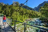 Frau wandert auf Hängebrücke über Routeburn Fluss, Routeburn Track, Great Walks, Fiordlands Nationalpark, UNESCO Welterbe Te Wahipounamu, Queenstown-Lake District, Otago, Südinsel, Neuseeland