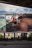 Mann auf Leiter bringt eine neue großformatige Werbeanzeige an, Belfast, Nordirland, Vereinigtes Königreich Großbritannien, UK, Europa