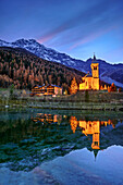 Beleuchtete Kirche von Sulden spiegelt sich in See mit Ortler im Hintergrund, Sulden, Ortlergruppe, Südtirol, Italien