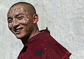 Tibetan Monk with white painting on his face while renovating the walls of a temple in Rongwo monastery, Tongren County, Longwu, China.