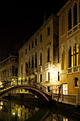 ITALY, Venice.  View of homes and bridge over a canal at night.