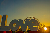A Large Sign Reading Love With A Silhouette Of A Ferris Wheel Against A Golden Sky At Sunset, Place Massena; Nice, Cote D'azur, France
