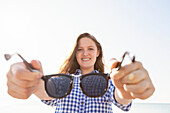 Girl offering her sunglasses by holding them out away from her towards the camera, Woodbine Beach; Toronto, Ontario, Canada