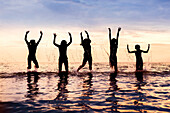 Silhouette of five children jumping out of the water in a row at sunset,Sandbanks Provincial Park; Picton, Ontario, Canada