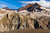 A man is dwarfed by the jagged, ash-covered Knife Creek Glaciers and Trident Volcano in the Valley of Ten Thousand Smokes in Katmai National Park; Alaska, United States of America