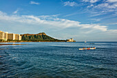 Tourists paddle in an outrigger canoe at Waikiki with Diamond Head in the distance; Waikiki, Oahu, Hawaii, United States of America