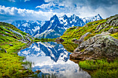 Aiguille des Charmoz, part of Aiguilles de Chamonix, reflects on Lac Flegere surrounded with green meadow, Aiguilles Rouges; Chamonix-Mont-Blanc, Haute-Savoie, France