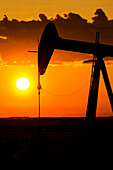 Silhouette Of A Pumpjack At Sunrise With A Colourful Orange Sun, Clouds And Sky; Alberta, Canada