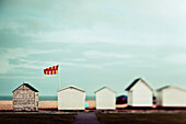 Small wooden buildings in a row on the beach with a view of the ocean; England