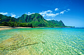 Clear turquoise ocean water and the rugged mountainous landscape on the island of Kauai; Kapaa, Kauai, Hawaii, United States of America