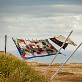 A patchwork blanket and pillow cases hanging on a clothesline with the Atlantic ocean in the background; Newfoundland, Canada