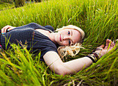Portrait of a young woman with long blond hair laying on the grass in a park; Edmonton, Alberta, Canada