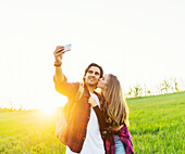 Young couple in a park posing for a self-portrait with their cell phone; Edmonton, Alberta, Canada