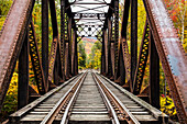 Iron railroad bridge over Sawyer River with trees in autumn colours, White Mountains National Forest; New England, United States of America