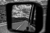 View of the highway and mountains,behind from a vehicle's rear view mirror out the side of the driver's door