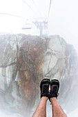 Personal perspective shot of man wearing running shoes riding Peak Chair chairlift on Whistler Backcomb, Whistler, British Columbia, Canada