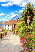 House of the village of Tirolo with flowers and crucifix, Merano, Sudtirol, Italy