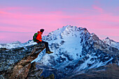 An hiker on a rock admiring Piazzi peak at sunset, Valdidentro, Valtellina, Lombardy, Italy