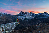 An hiker on a rock in Viola valley with a panoramic view at sunset, Valdidentro, Valtellina, Lombardy, Italy