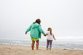 Caucasian mother and daughter holding hands on beach