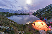 Hikers and tent on the shore of Lacs De Cheserys at night with Mont Blanc massif in background, Chamonix, Haute Savoie, French Alps, France, Europe